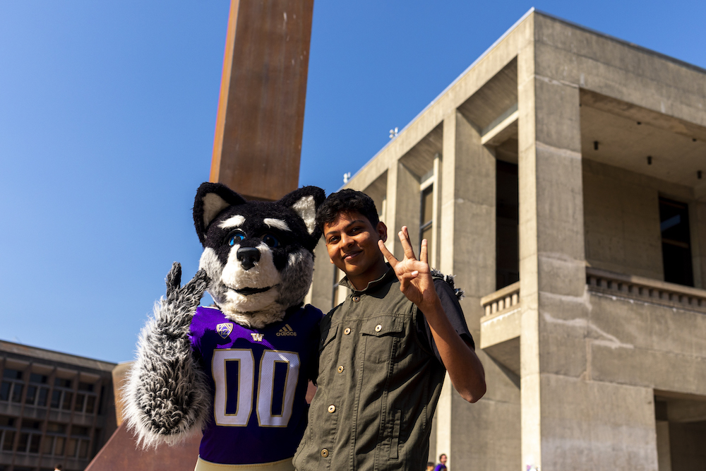 student posing with Harry the Husky